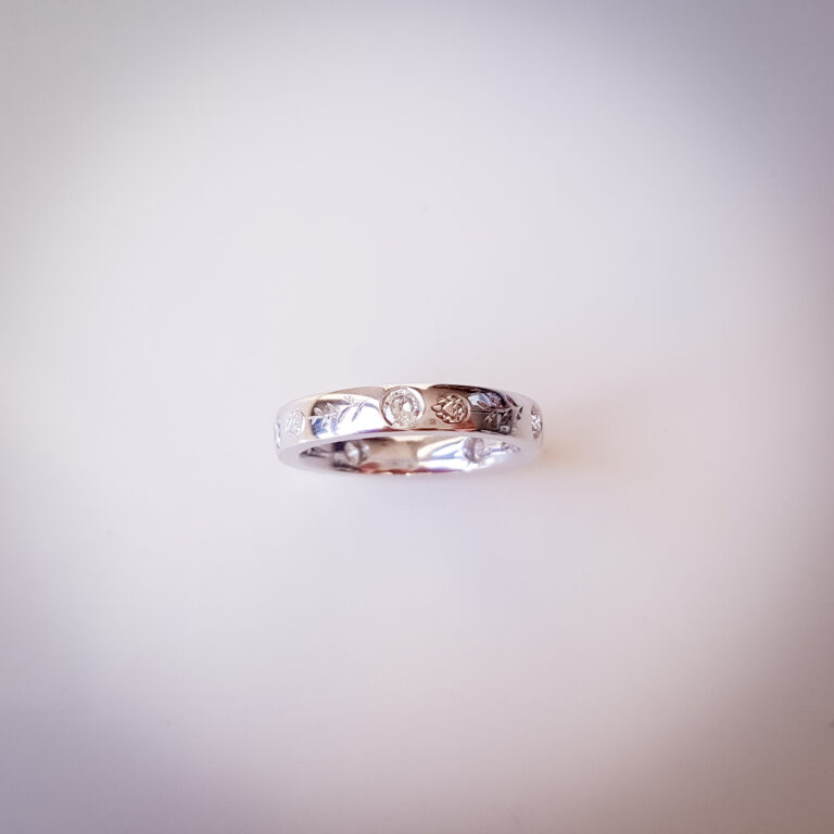 Platinum wedding band with flush-set diamonds, protea engraving on the outside and hummingbird engraving on the inside