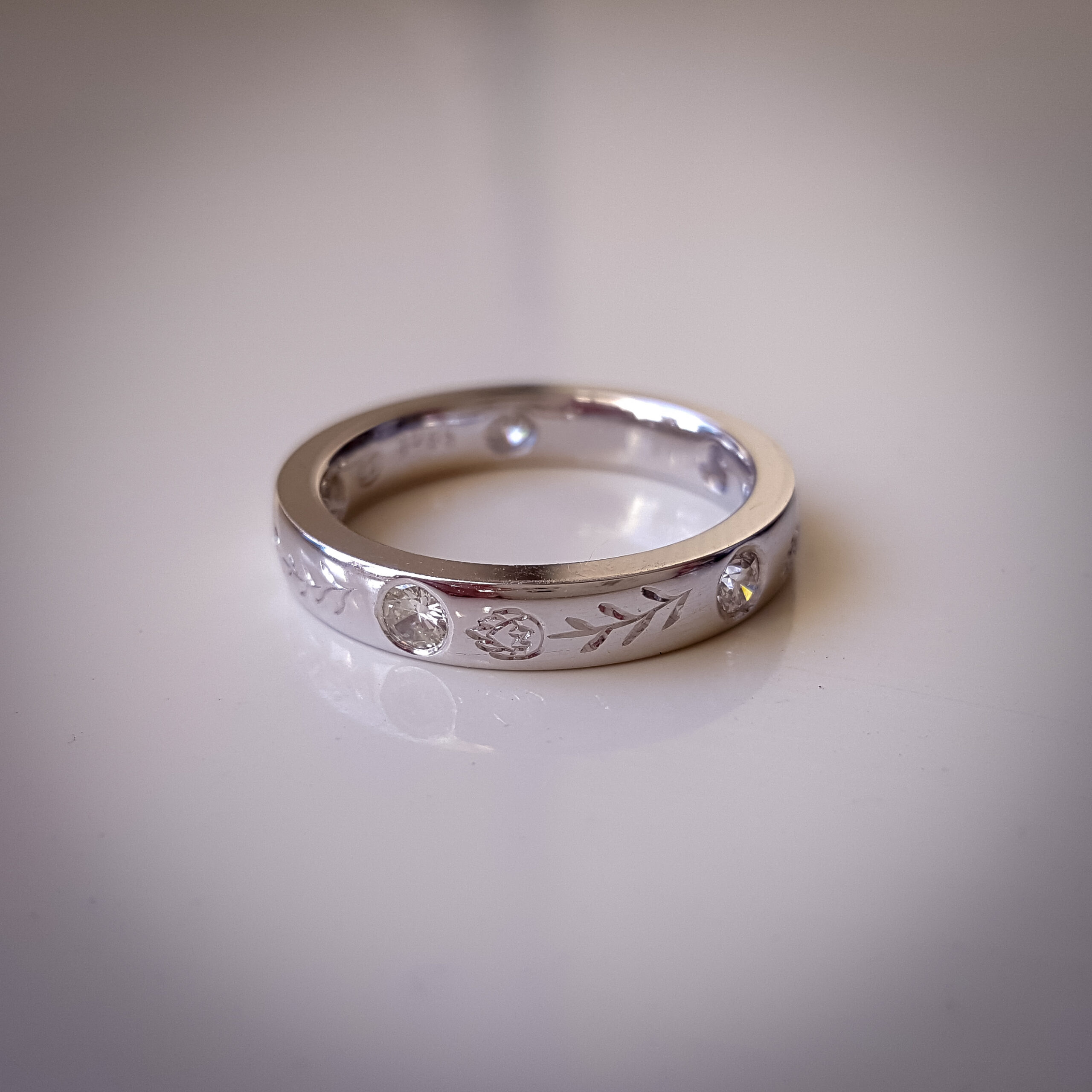 Platinum wedding band with flush-set diamonds, protea engraving on the outside and hummingbird engraving on the inside