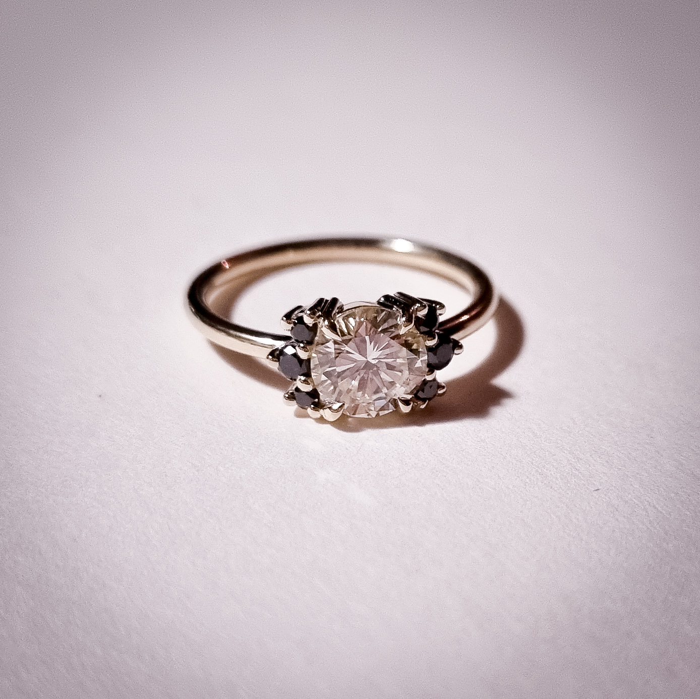 Yellow gold engagement ring with a round centre diamond and black diamond accents on either side