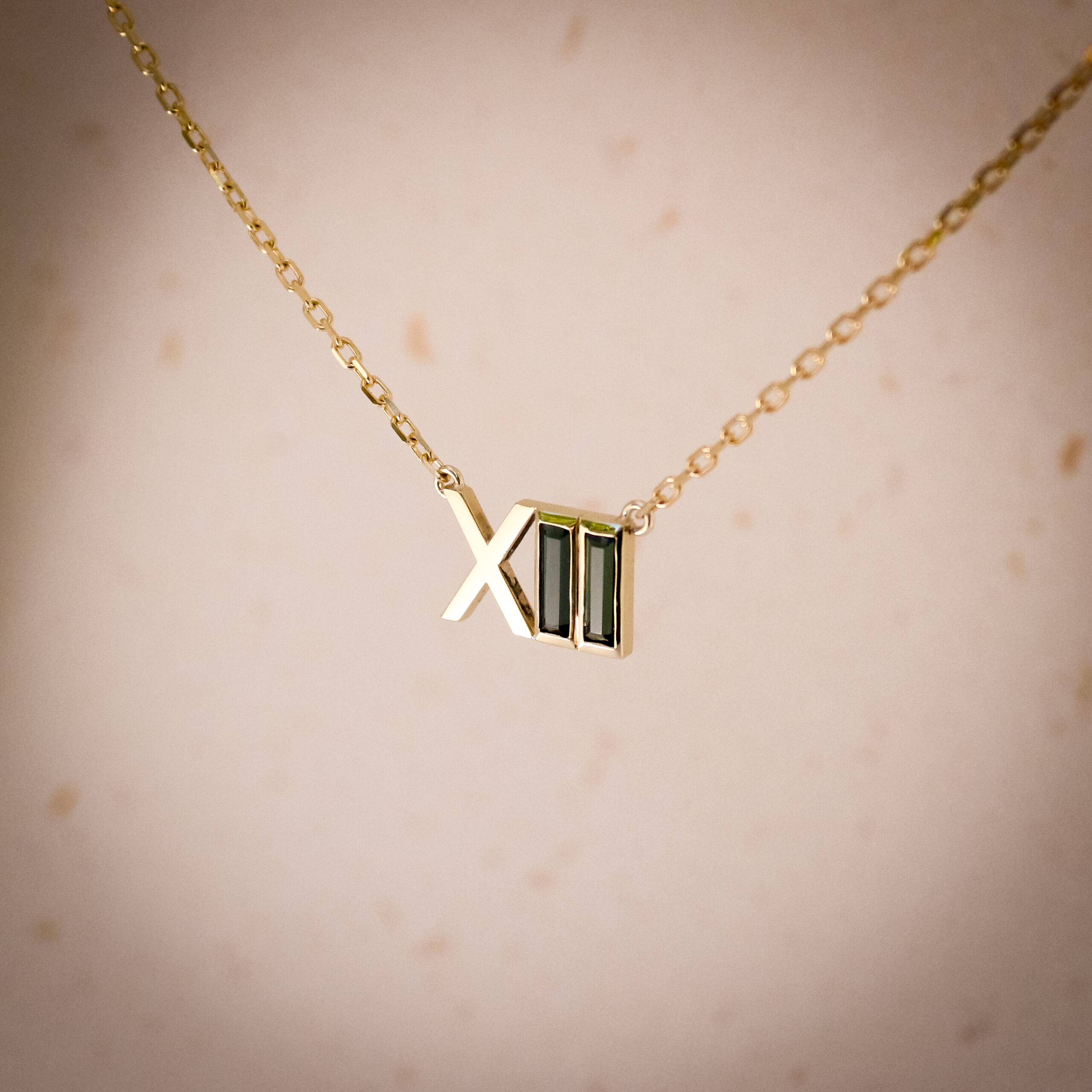 9k yellow gold Roman numeral pendant with green tourmaline baguette stones, suspended on a fine gold chain