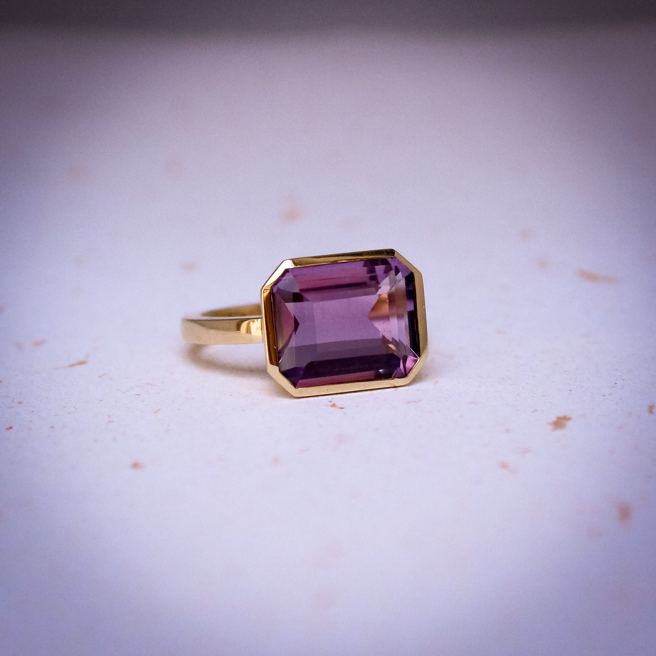 9k yellow gold ring set with a large emerald cut amethyst in a bezel setting