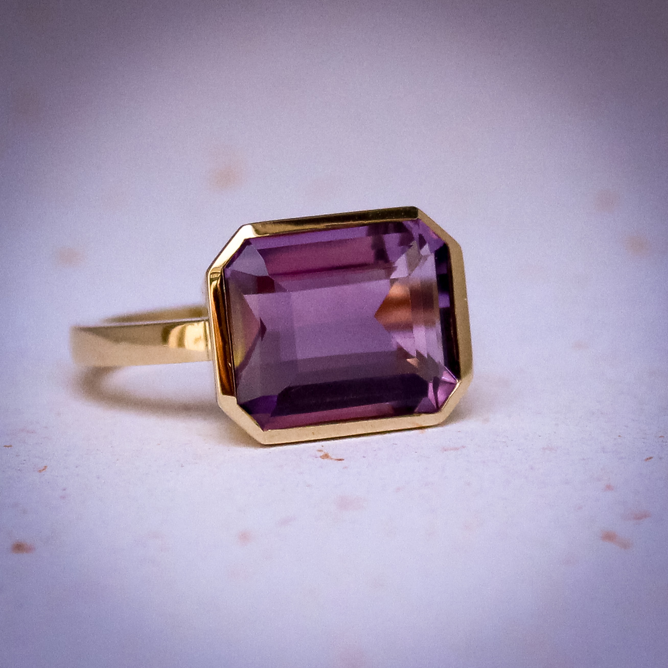 9k yellow gold ring set with a large emerald cut amethyst in a bezel setting