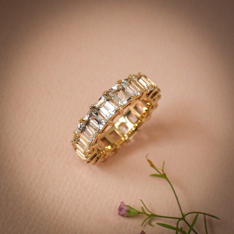 Full eternity ring set with emerald cut quartz crystals in 9k yellow gold on a soft neutral background