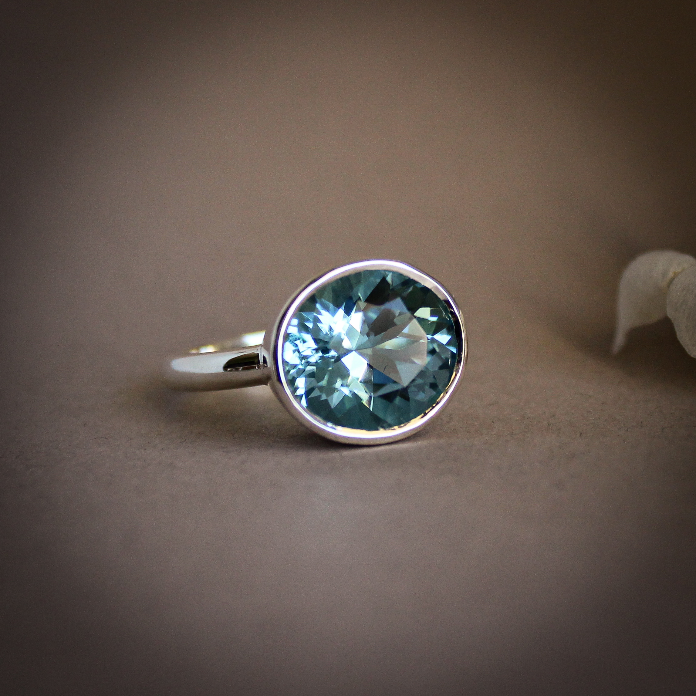Round aquamarine gemstone set in a smooth silver bezel setting on a minimalist ring